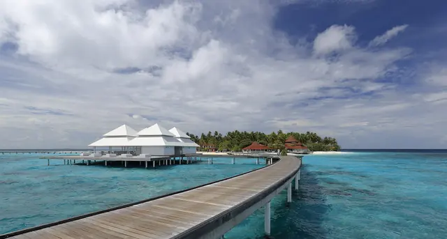 A wooden jetty leading to water villas over a turquoise Maldives lagoon